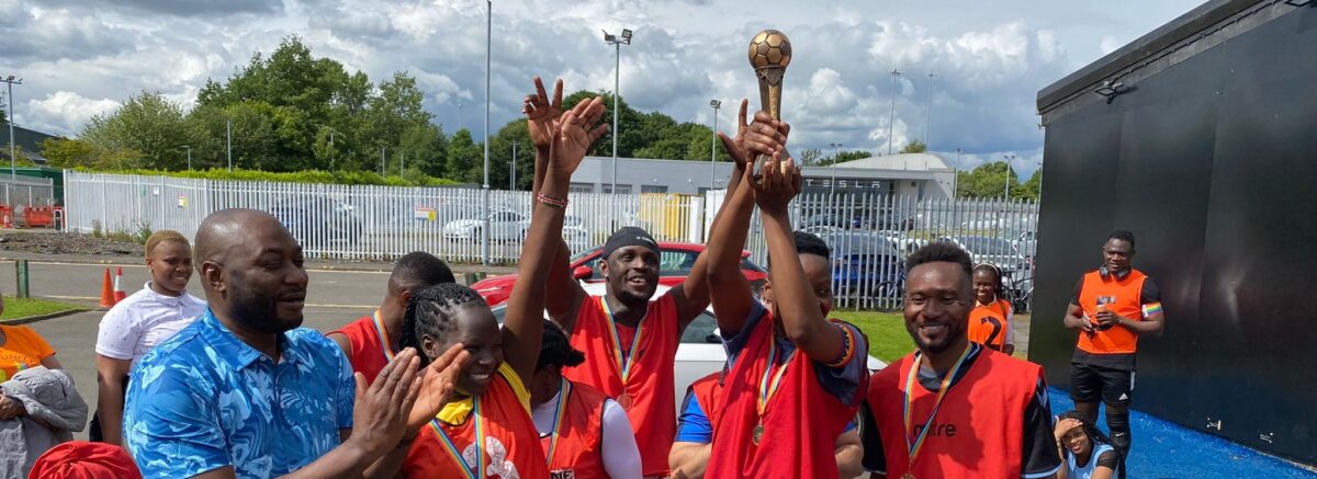 A group of people wearing red bibs and sports clothing holding up a trophy and celebrating.